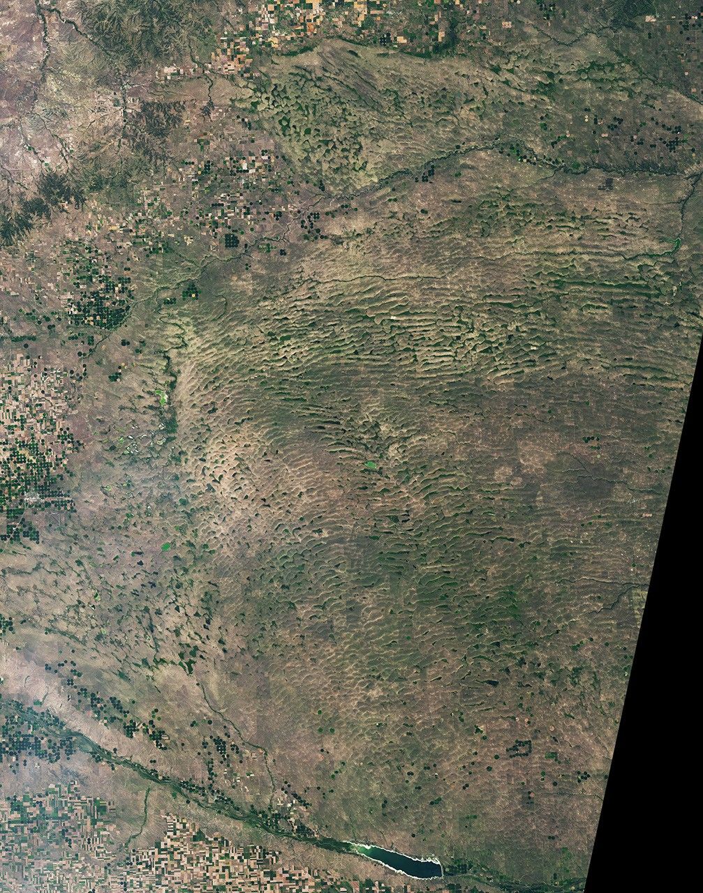 The landscape in northwestern Nebraska has a rippled appearance, with tan parallel ridges running from left to right and green areas and small lakes filling the low-lying spaces in between.