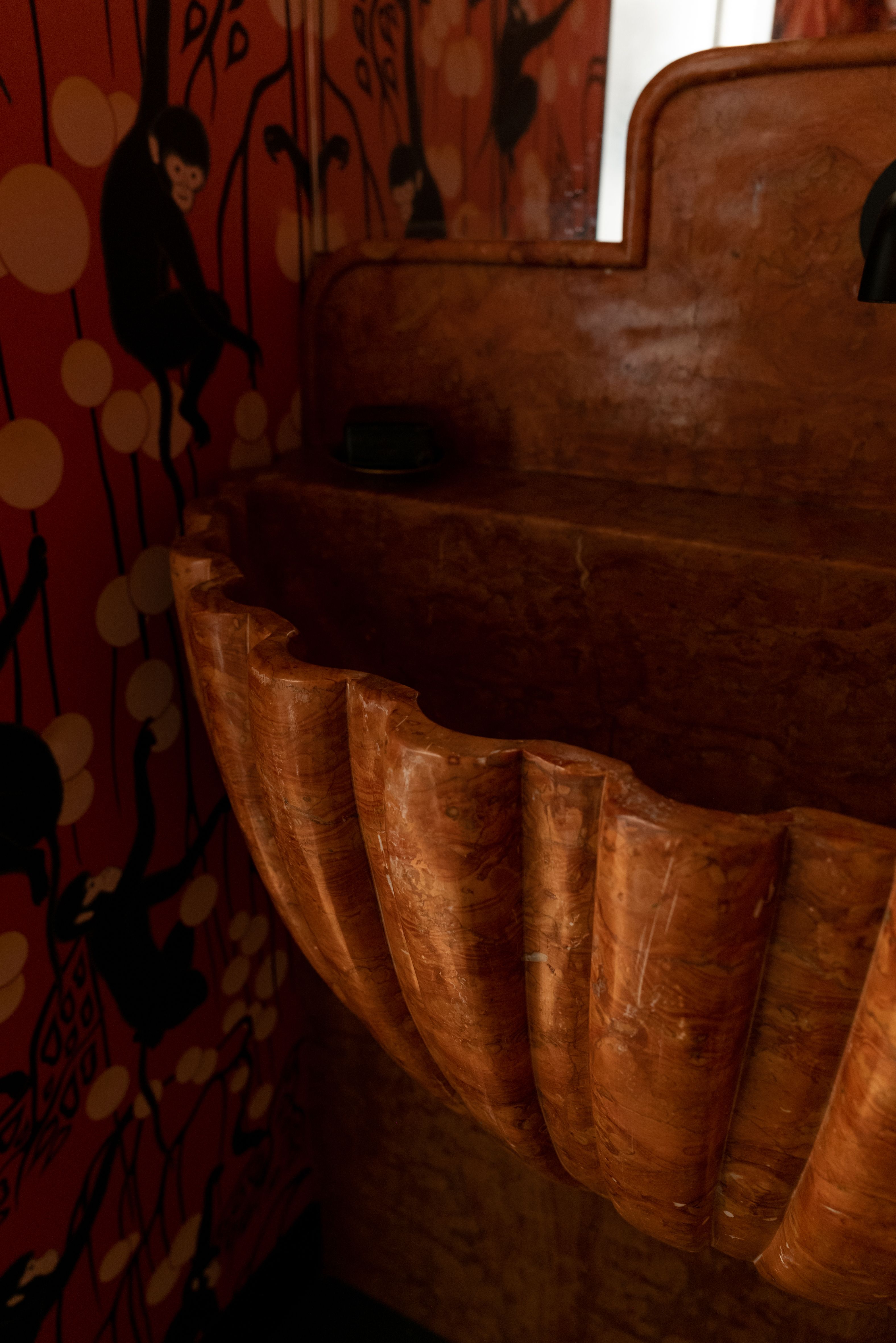 A close up of an elaborate basin in a deep orange with orange patterned wallpaper with monkeys on it