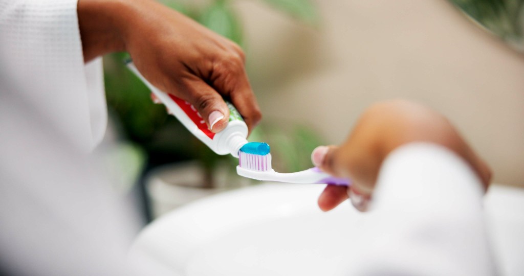 A person squeezing blue toothpaste onto a toothbrush over a sink.