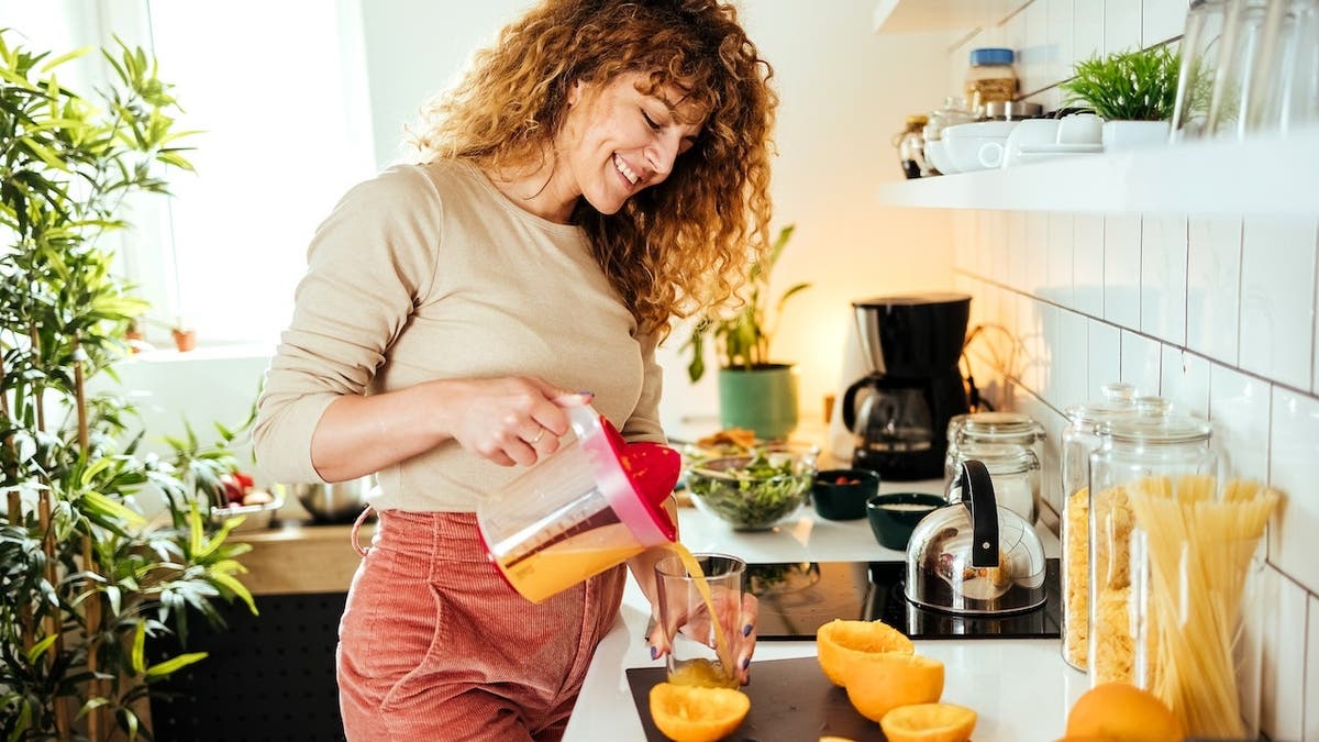 Woman's hands pouring freshly squeezed orange juice into a glass.