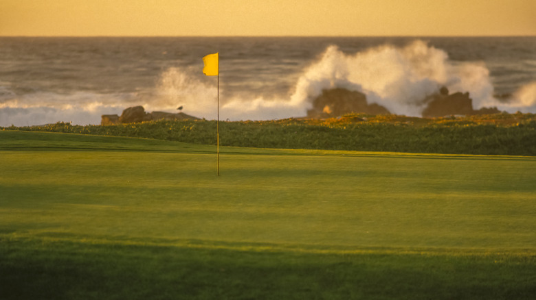 Close up view of the flag on a green at Pebble Beach Golf Links with Pacific Ocean waves crashing in the background