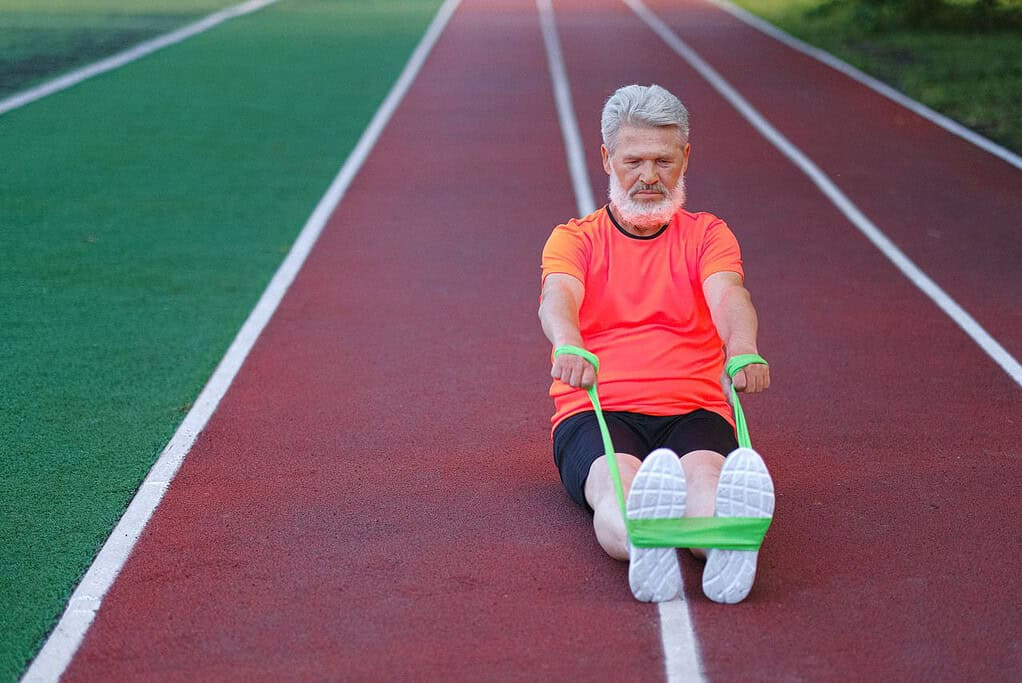 Senior man doing resistance band exercise on running track.