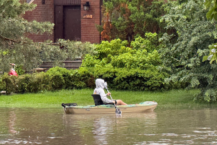 Man paddles a canoe in floodwaters outside a home.