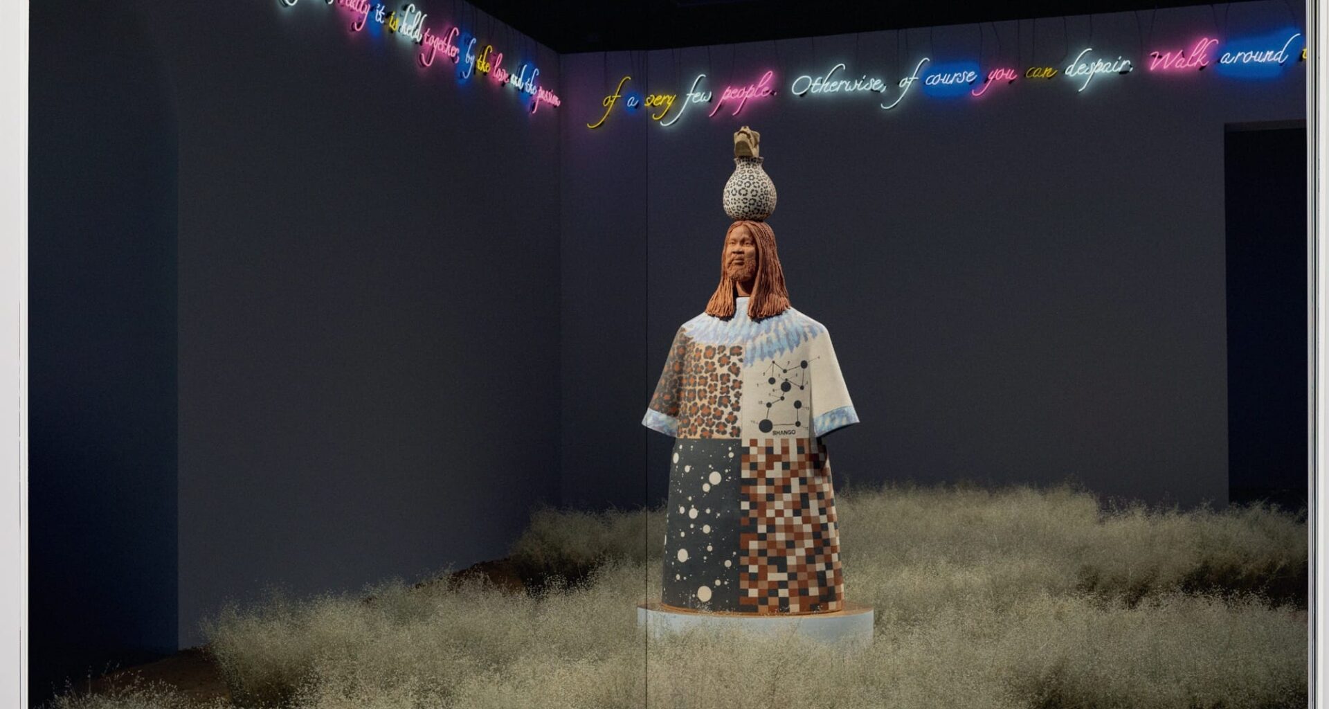 an open book spread with a grassy installation surrounding a figurative sculpture with neon text around the room