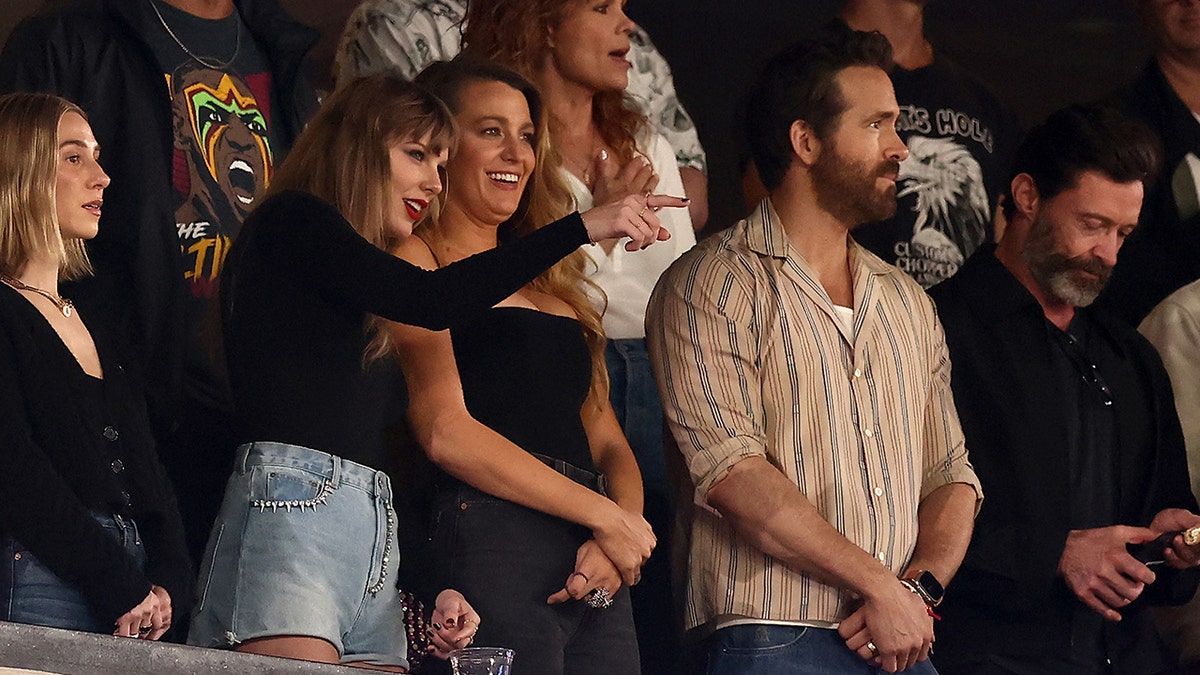 Taylor Swift points at the field next to Blake Lively, Ryan Reynolds and Hugh Jackman at a game.