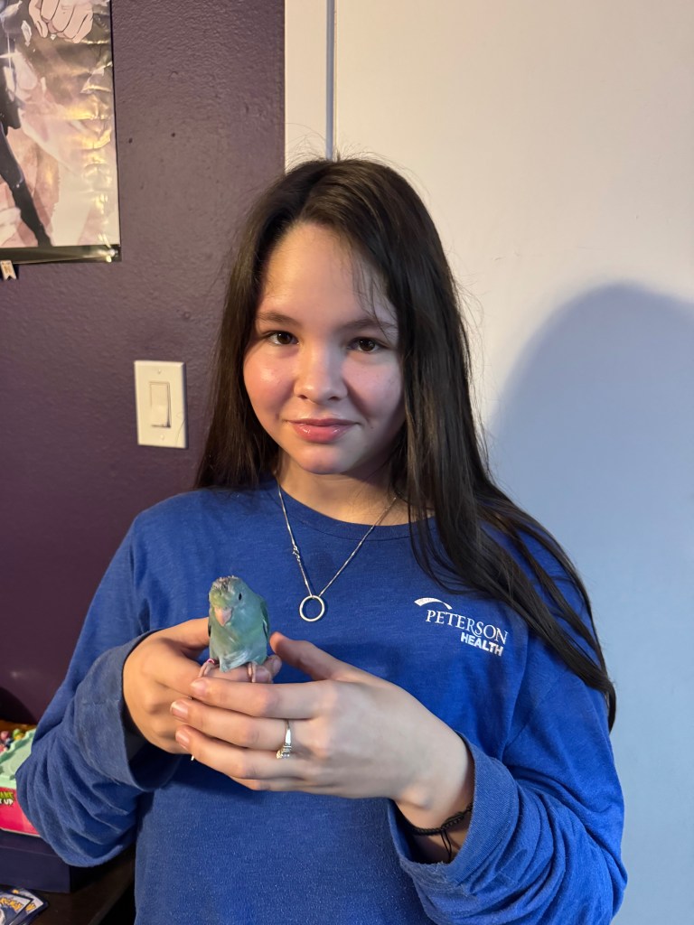 Kaydin Ruiz holding a light blue parakeet in her hands.