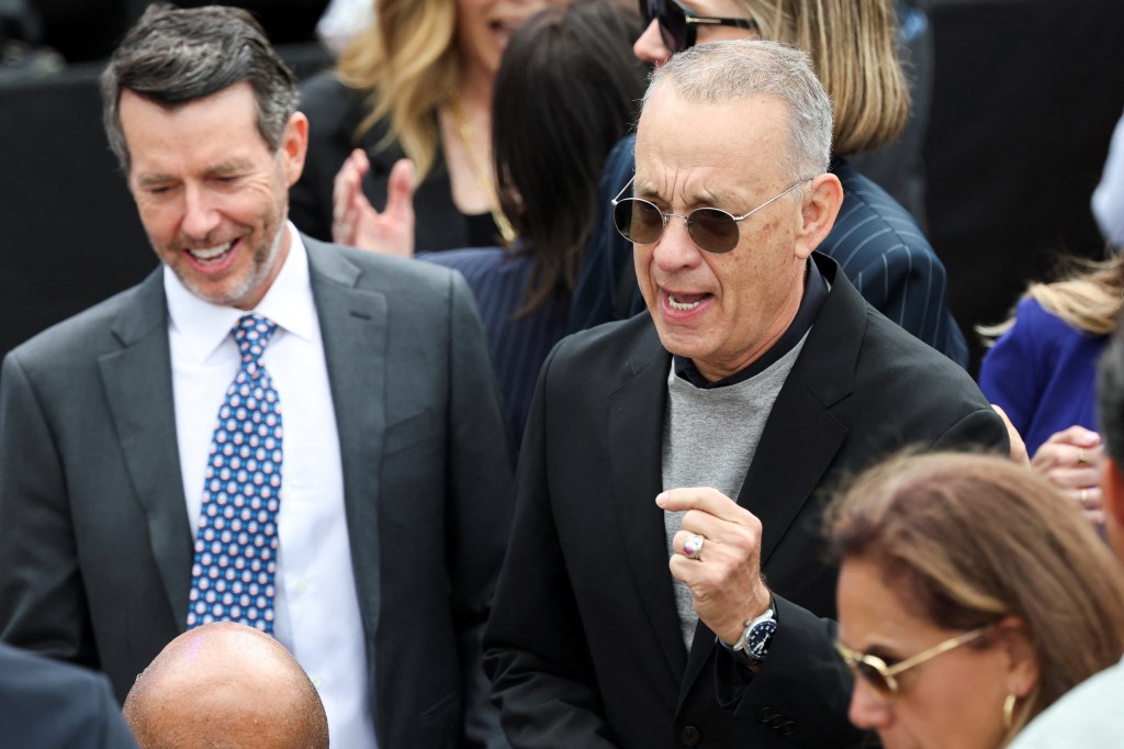 Tom Hanks speaking while a man in a suit laughs beside him at the Obama Presidential Center dedication ceremony.