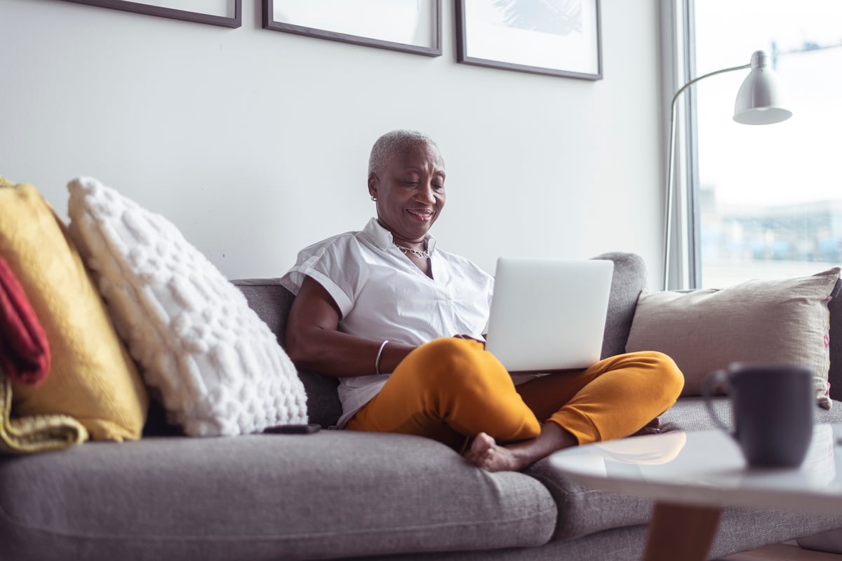 Smiling person using laptop on couch.
