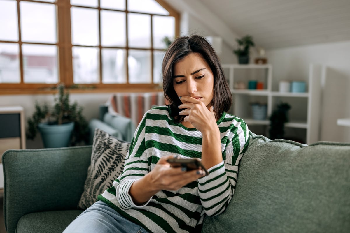 Thinking person with hand on chin looking at smartphone.