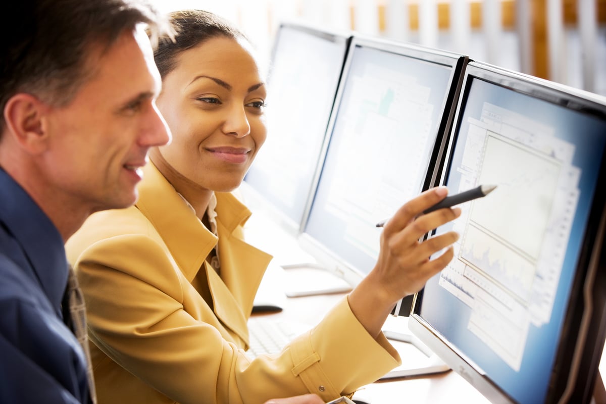 An investor points something out to another investor on a computer screen.