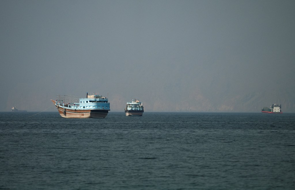Several vessels on the water at the Strait of Hormuz, with faint land in the background.