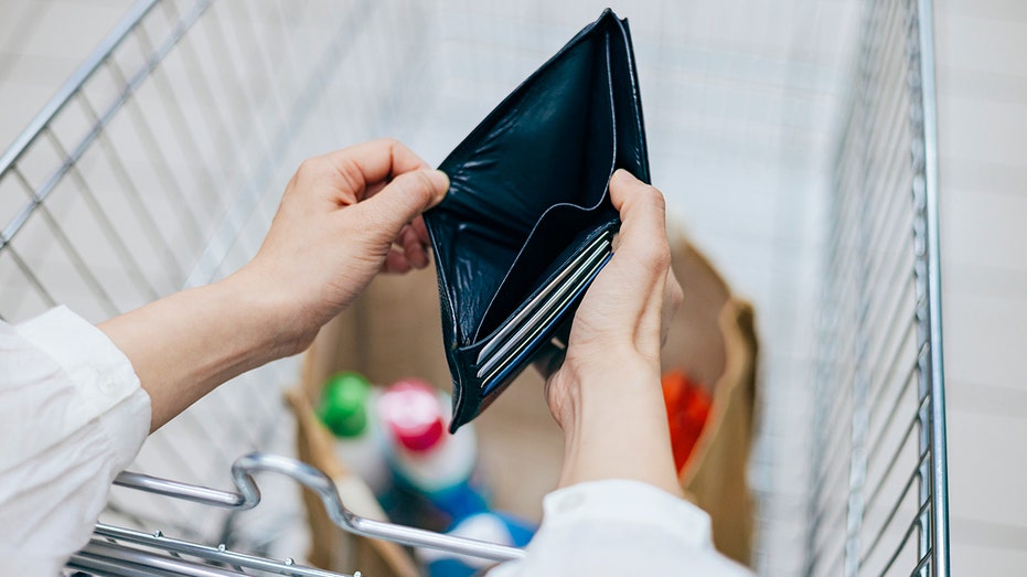 Woman holds empty wallet over shopping cart