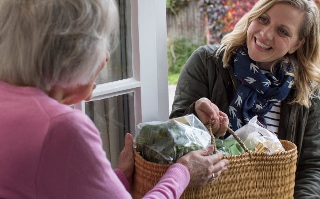 Woman helping elderly neighbour with groceries 