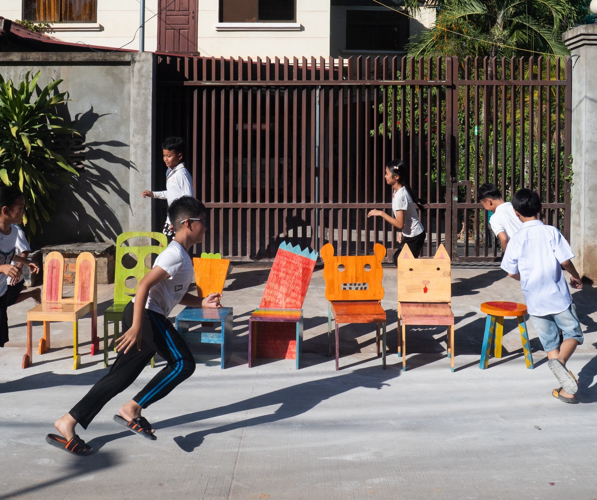 children run around a series of colorful, whimsical chair designs conceived by children and created by Taekhan Yun