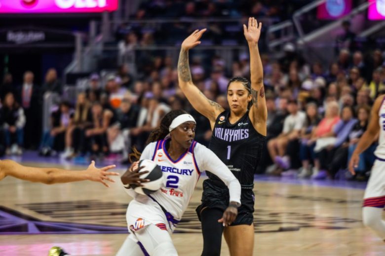 A basketball player from the Mercury prepares to shoot while being closely defended by a Valkyries player during a game, with spectators in the background.