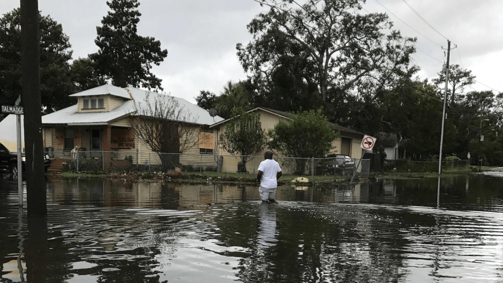 A person stands in knee-deep water during a flood in front of a house.