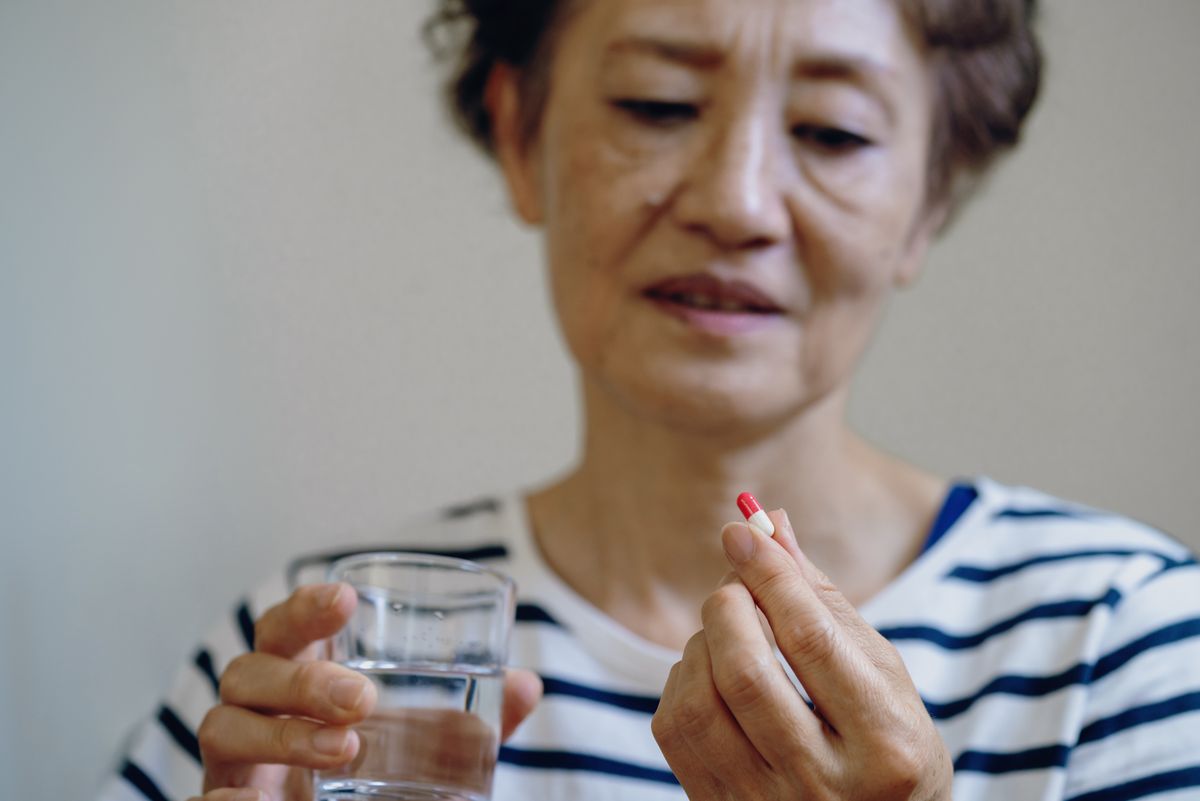 Senior woman sitting at a kitchen table is taking medicine