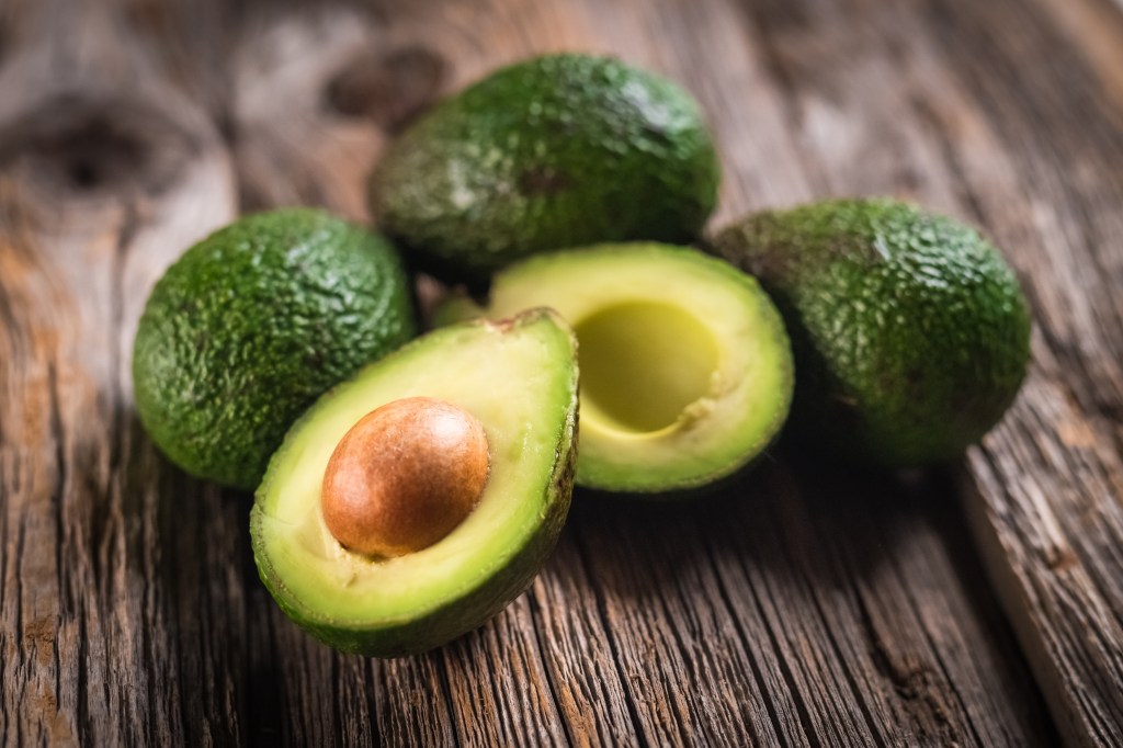 Avocado halves and whole avocados on a wooden surface.