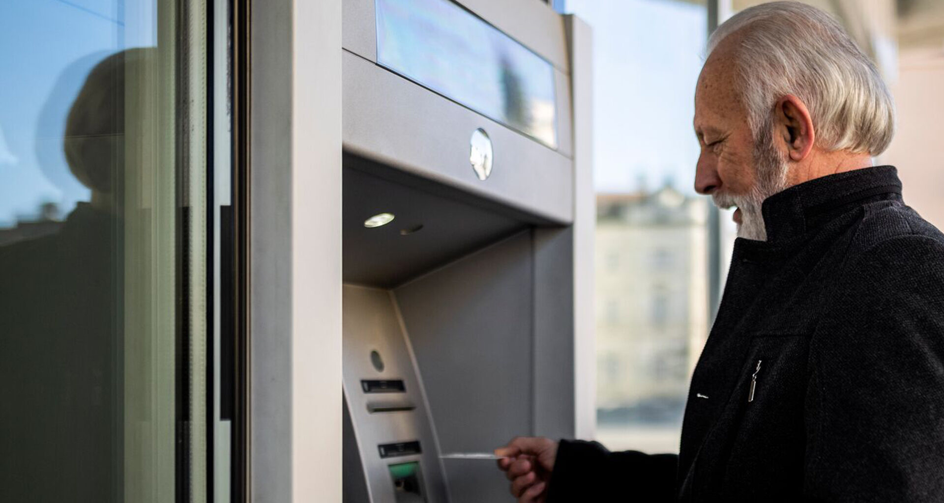 An older man who is using his credit card at an atm.