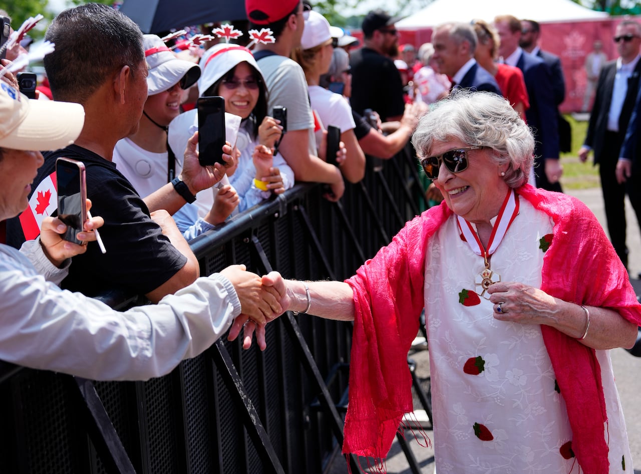 A woman dressed in white shakes hands with people in a crowd.