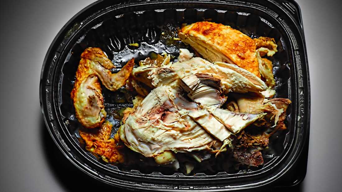 Close-up eaten chicken leftovers in black lunch box on gray background
