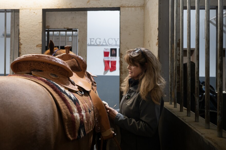 A woman stands next to a horse in a stall.