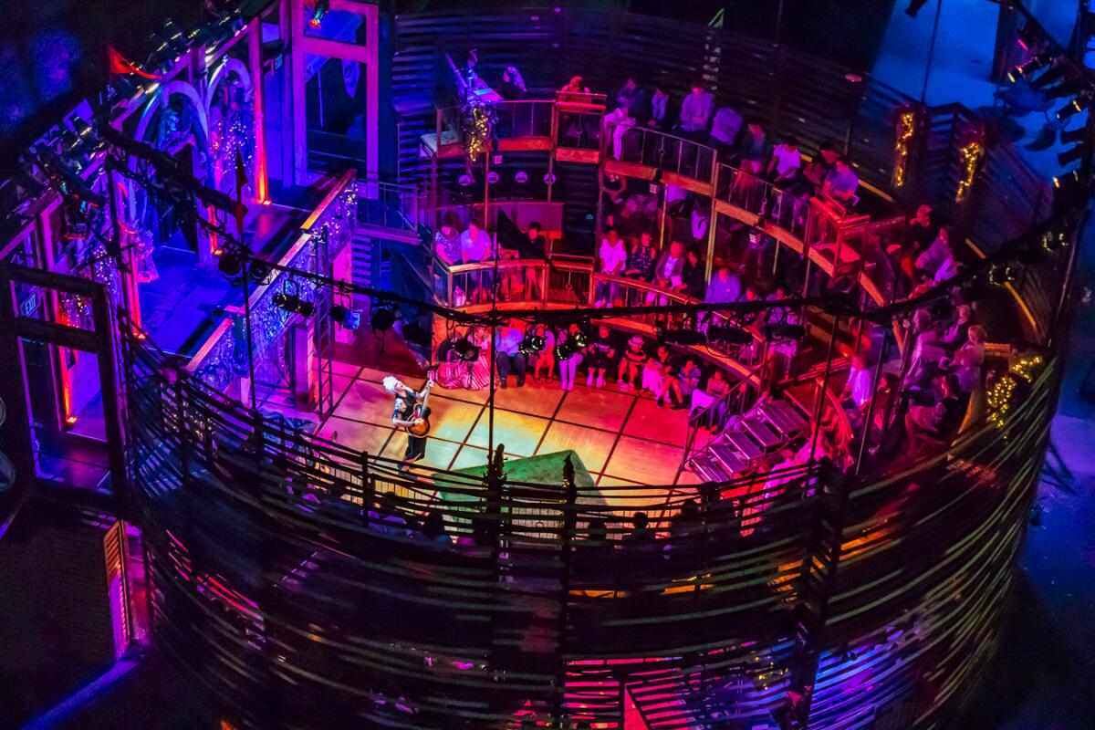A nighttime aerial view of a brightly lit outdoor thrust theater stage.