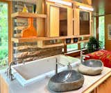 The primary suite has an open bedroom-and-bath layout with views of the ravine and Zen garden. Features include an air-jet tub, a glass-block shower wall, carved granite sinks, custom birch veneer cabinetry, and a walk-in closet/laundry room with an Electrolux washer and dryer.