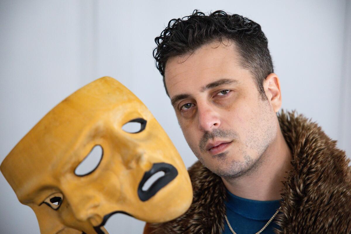 A man holds a three-faced mask.