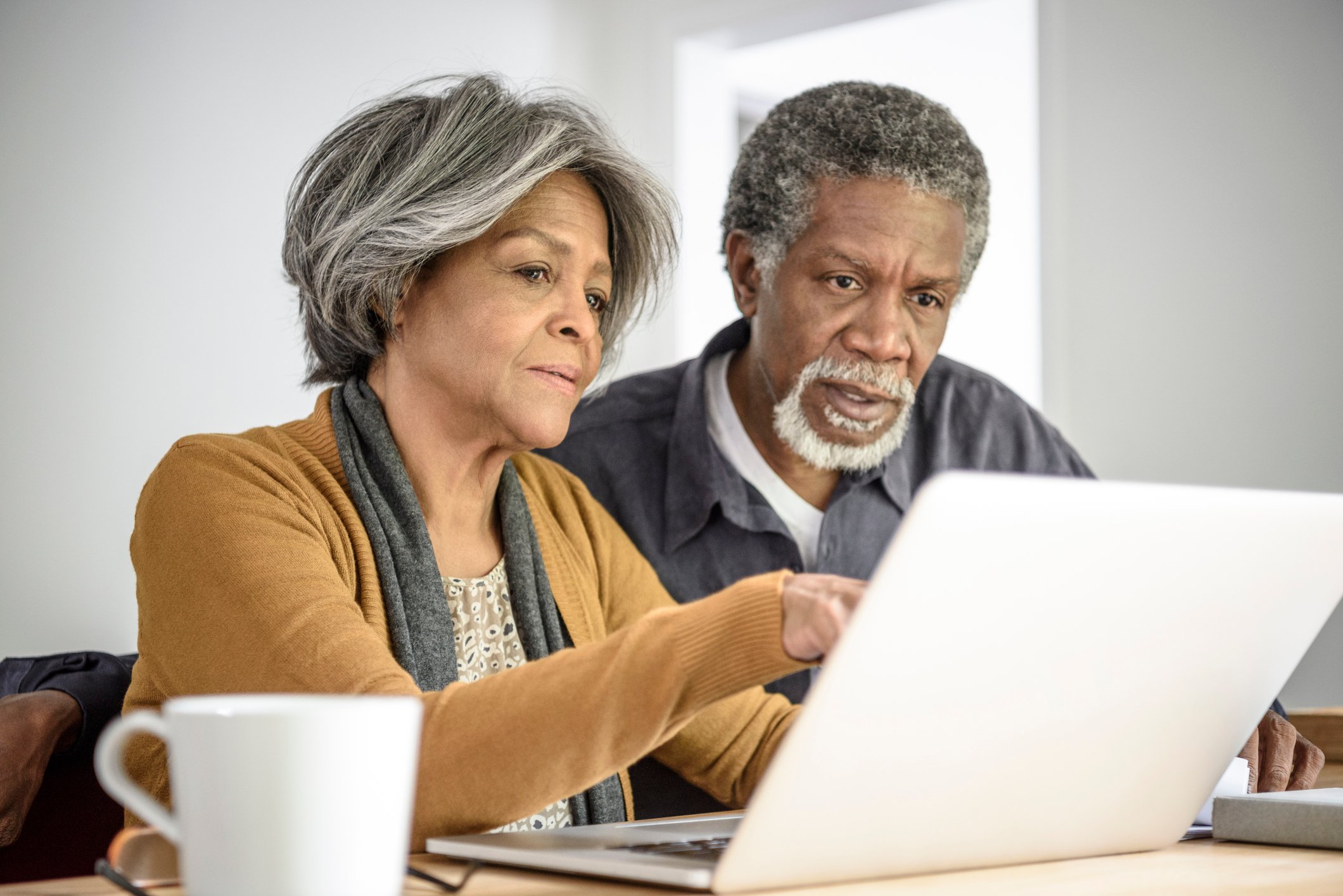 A couple intently reading content from a shared laptop while seated at a table in their home.