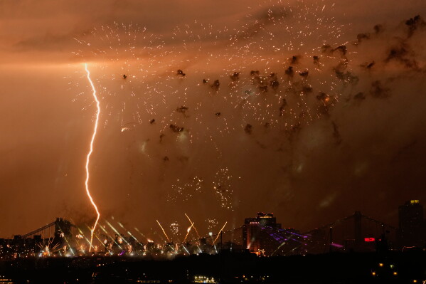 A bolt of lighting strikes as fireworks are set off of the Brooklyn Bridge, as seen from Bayonne, N.J., Saturday, July 4, 2026. (AP Photo/Seth Wenig)