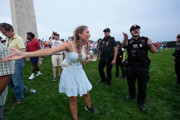 An attendee asks questions to U.S. Park Police officers as they evacuate attendees due to severe weather during a Salute to America Independence Day event honoring the nation's 250th anniversary, Saturday, July 4, 2026, on the National Mall in Washington. (AP Photo/Manuel Balce Ceneta)