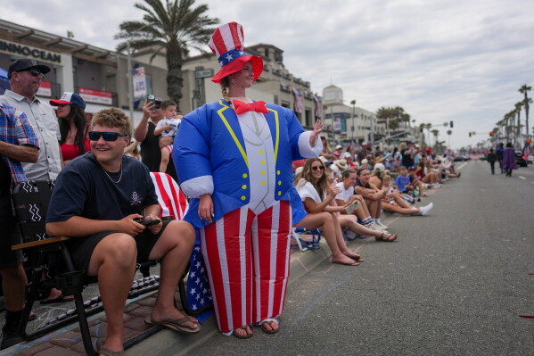 Madyson White wearing an inflatable Uncle Sam costume waves while watching an Independence Day parade in Huntington Beach, Calif., Saturday, July 4, 2026. (AP Photo/Jae C. Hong)