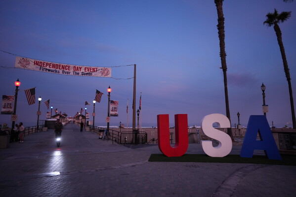 A person rides a scooter past a large "USA" installation on Independence Day in Huntington Beach, Calif., Saturday, July 4, 2026. (AP Photo/Jae C. Hong)