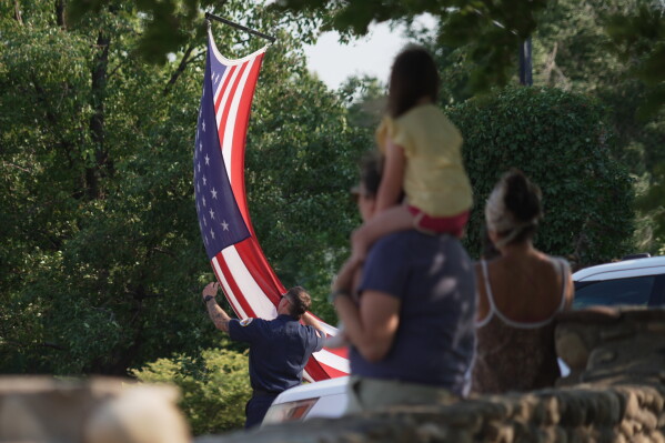 A first responder adjusts an American flag during a procession in Grand Junction, Colo., Monday, June 29, 2026, for firefighters who died battling blazes near the Colorado-Utah border. (AP Photo/Ty ONeil)
