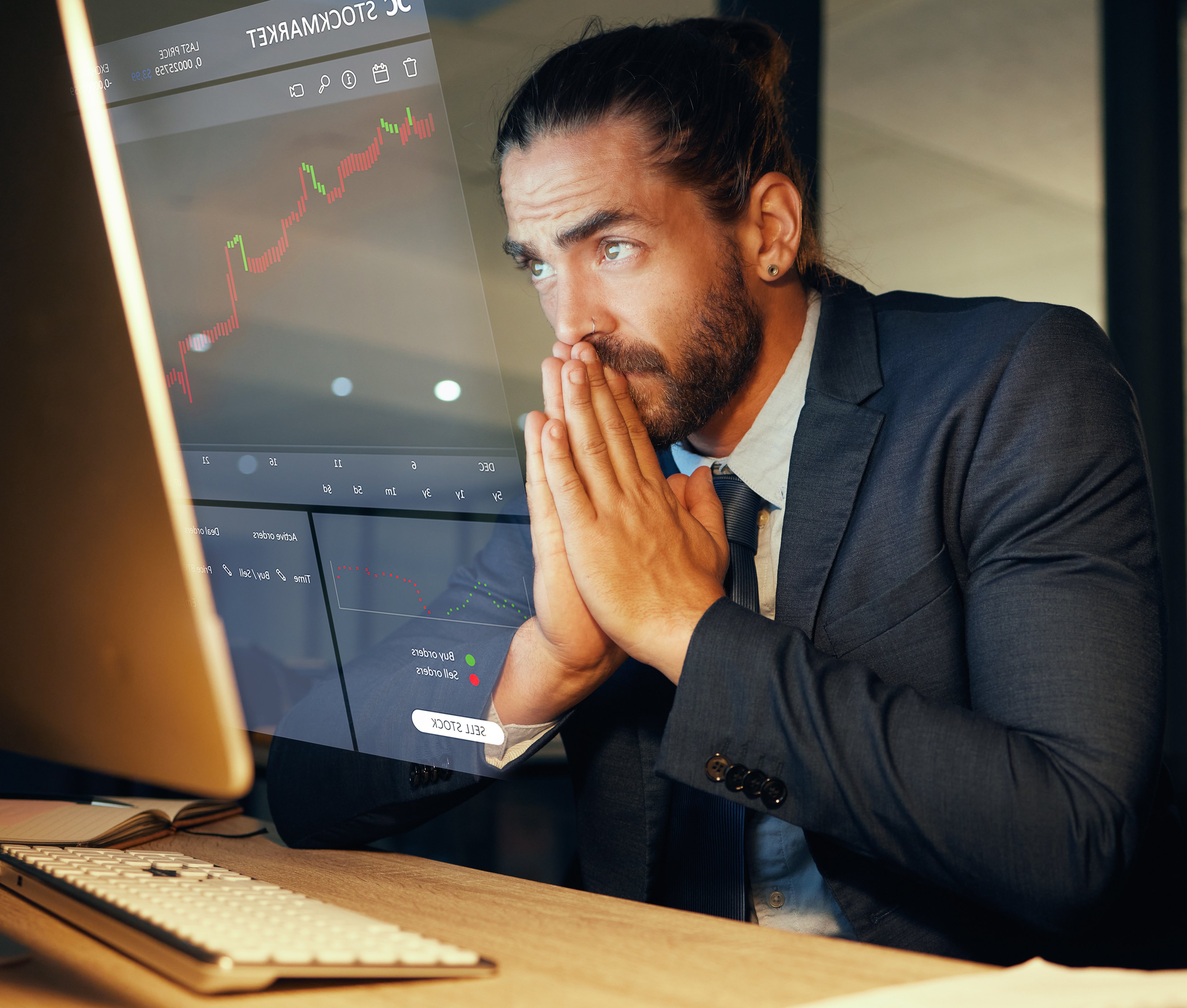 Person in a suit looking at a computer screen with folded hands.