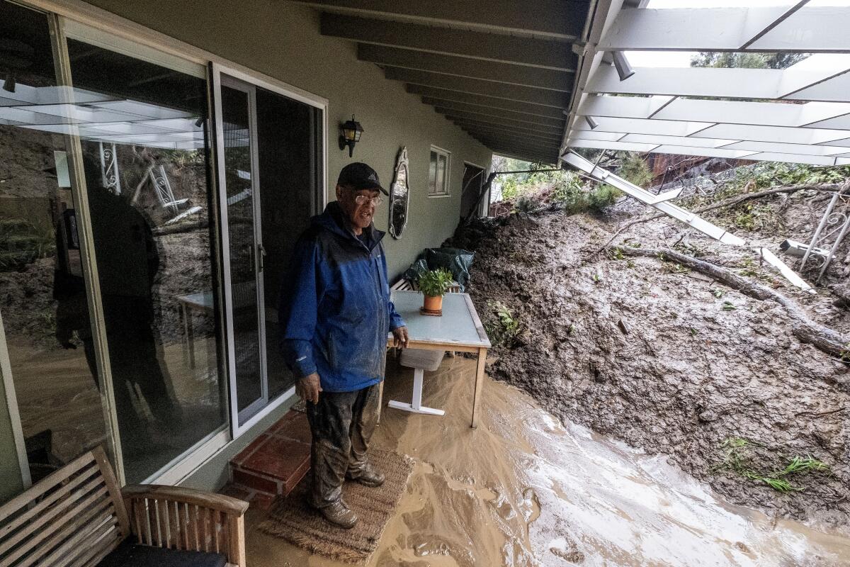 A man wearing a rain jacket and muddy shoes examines a mound of mud in his backyard