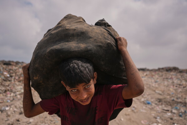 Omar Ghabin, 14, looks at the camera as he carries a bag of items he collected from the landfill in Deir al-Balah, central Gaza Strip, Thursday, July 23, 2026. (AP Photo/Abdel Kareem Hana)