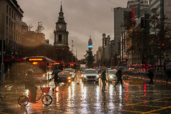 People cross Alameda Bernardo O'Higgins Avenue during a rainstorm in Santiago, Chile, early Monday, July 20, 2026. (AP Photo/Esteban Felix)