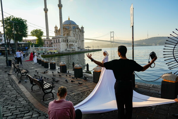 Photographer Enes Khazam works during a photo session on the bank of the Bosphorus Strait, with the Ortakoy mosque and 15th July Martyrs bridge in the background in Istanbul, Turkey, early Friday, June 26, 2026. (AP Photo/Emrah Gurel)