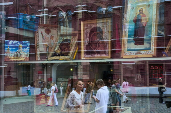 People are reflected in the window of an icon shop on Red Square near the Church of the Kazan Icon of the Mother of God in Moscow on Tuesday, July 21, 2026, the feast day of the Kazan Icon of the Mother of God. The Kremlin Wall and the Spasskaya Tower are in the background at left. (AP Photo/Alexander Zemlianichenko)