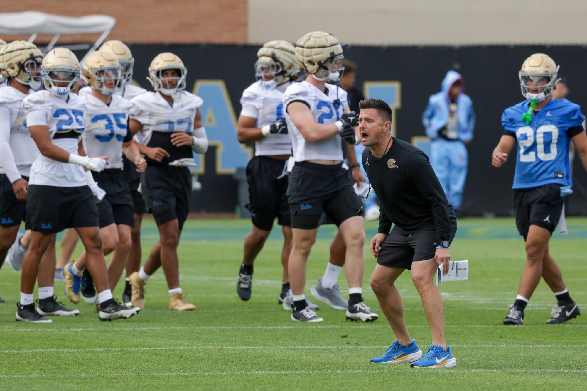 UCLA coach Bob Chesney stands on the field in between players and shouts instructions during a spring practice.
