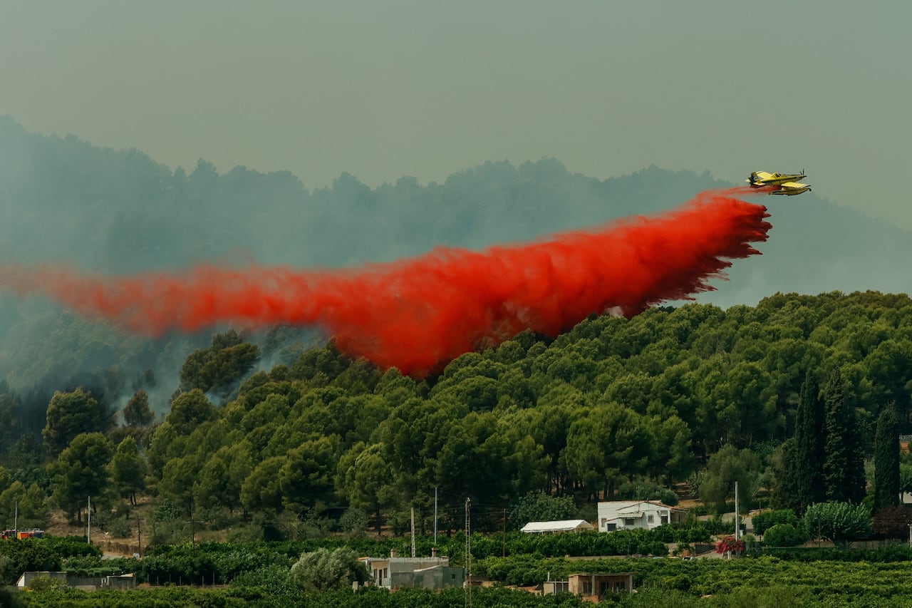 A plane drops fire retardant, which appears as a red cloud.