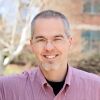 This photo is a head shot of Wil Davenport in 2015. He's wearing a purplish shirt and wire-frame glasses and has a goatee.