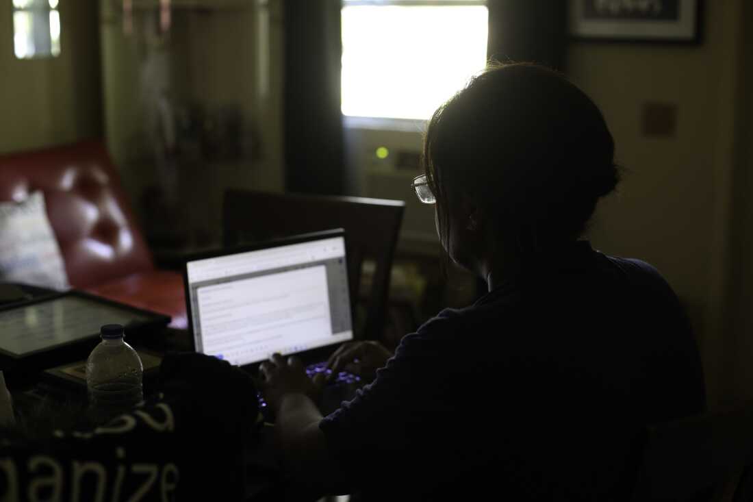 Photographed from behind, Farah Larrieux sits in front of her laptop computer in her South Florida home.