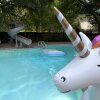 A swimming pool with a slide and an inflatable unicorn, raft and floatation tubes.