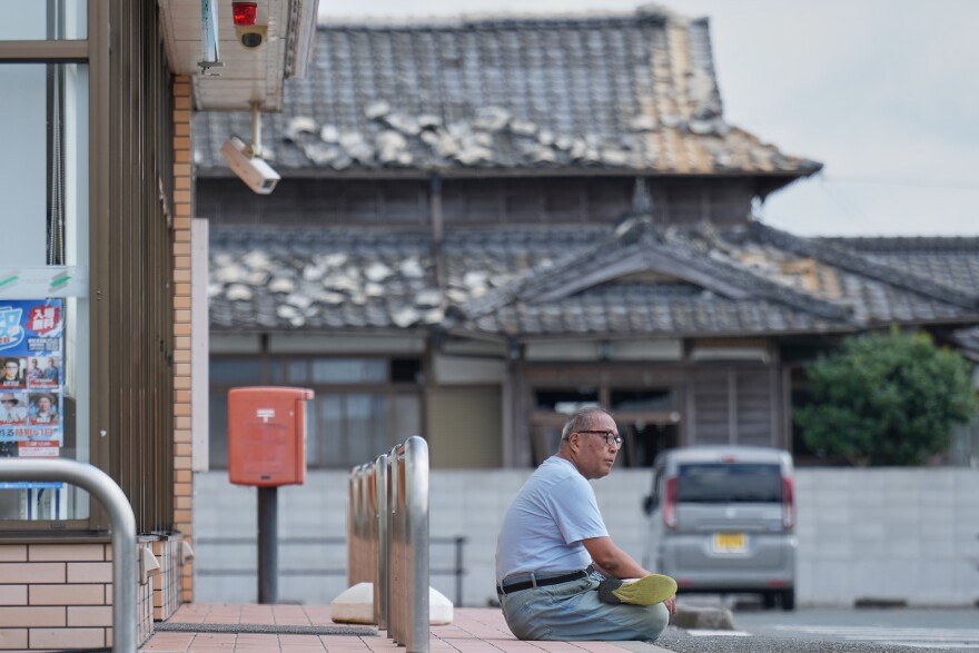 A person sits near a house damaged following an earthquake in Uki, Kumamoto Prefecture, southern Japan, Thursday, July 30, 2026.