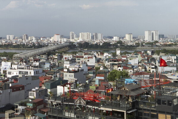 A view of Hanoi showing the Red River, with a bridge spanning the river and densely populated neighborhoods lining its banks. Hanoi, Vietnam, Wednesday, June 24, 2026. (AP Photo/Aniruddha Ghosal)

