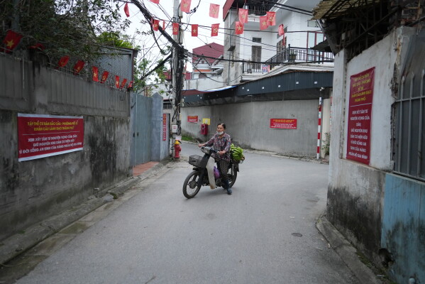 A woman rides a moped past banners put up by local residents to call for stopping a project that would displace the entire village by the Red river in Hanoi, Vietnam, Thursday, June 11, 2026. (AP Photo/Hau Dinh)
