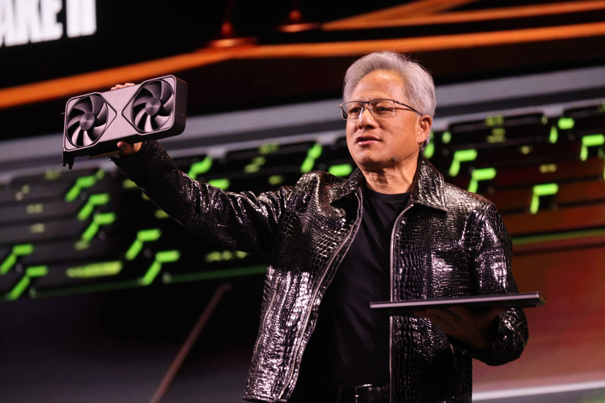 Jensen Huang is holding up a GPU in front of an audience.